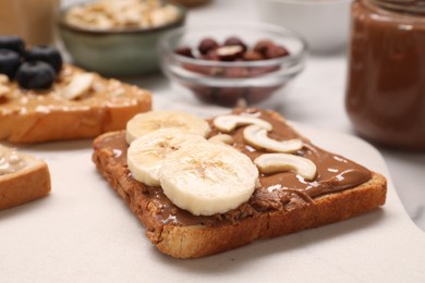 Photo of Toast with nut butter, banana slices and cashews on white table, closeup