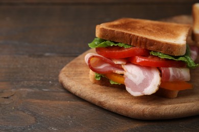 Photo of Tasty sandwich with bacon and tomato on wooden table, closeup. Space for text