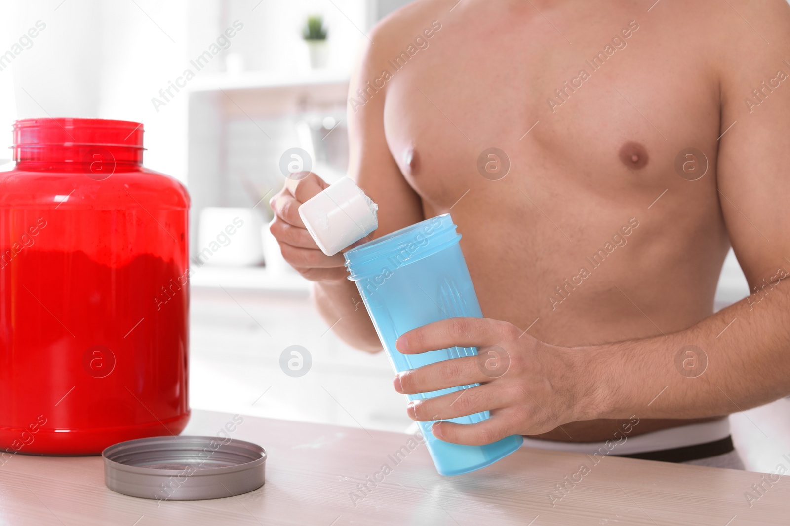 Photo of Young shirtless man preparing protein shake at table in kitchen, closeup