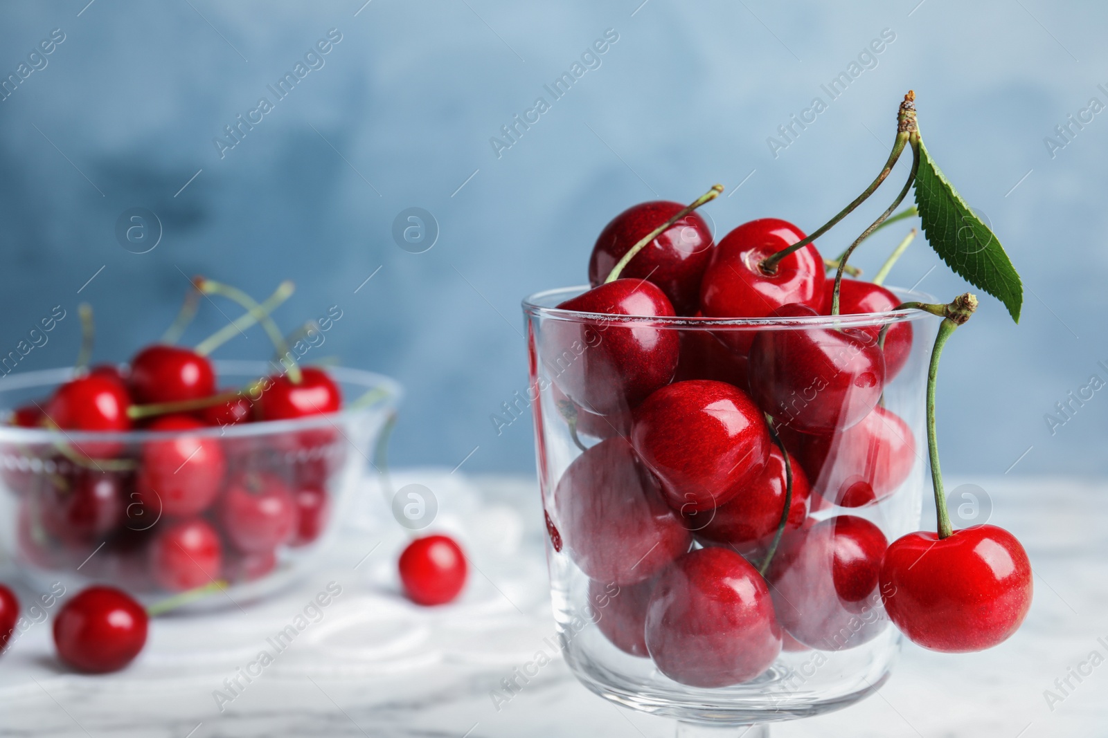 Photo of Glass dessert bowl with ripe sweet cherries on marble table. Space for text