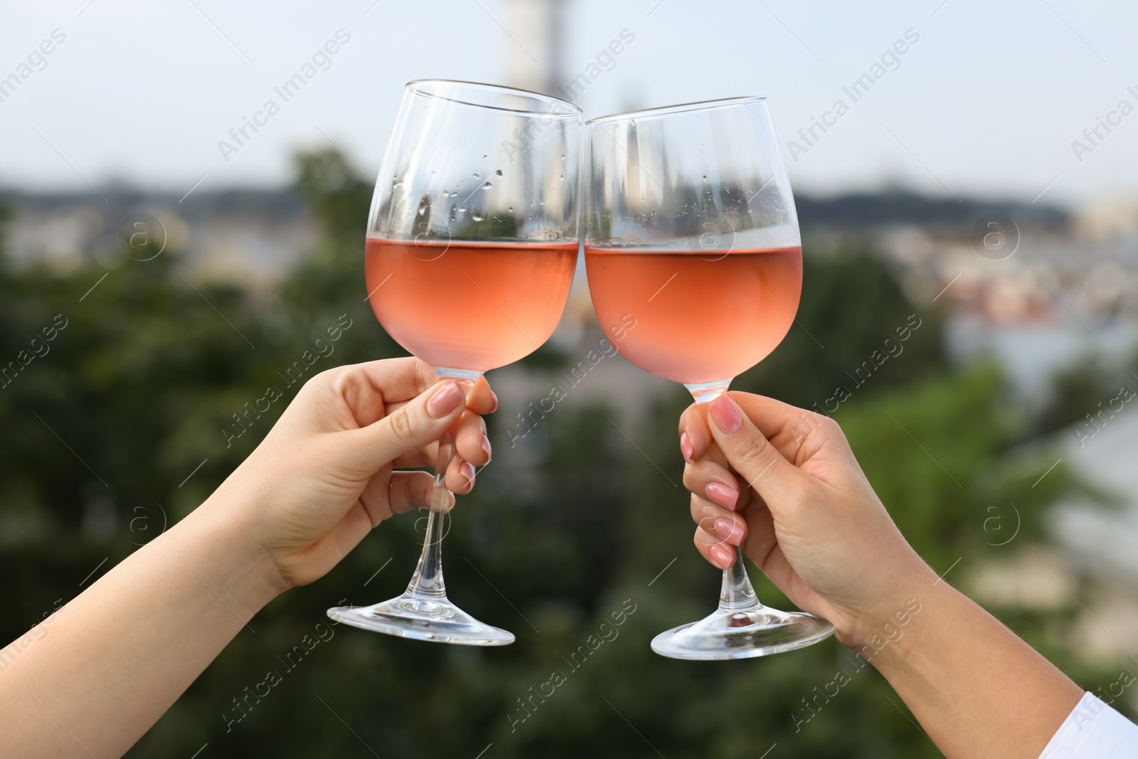 Photo of Women clinking glasses with rose wine outdoors, closeup