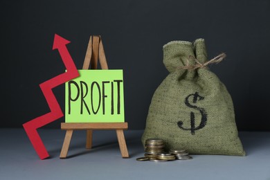 Photo of Economic profit. Money bag, arrow, coins and easel with note on grey table