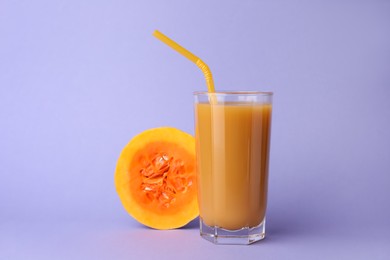 Photo of Tasty pumpkin juice in glass and cut pumpkin on lavender color background