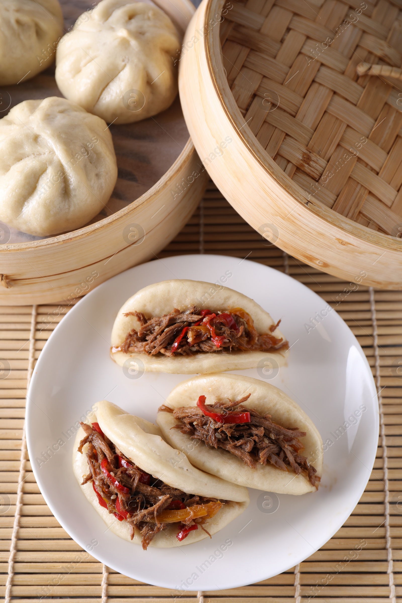 Photo of Plate with delicious gua bao (pork belly buns) and bao buns (baozi) on bamboo mat, top view