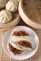 Plate with delicious gua bao (pork belly buns) and bao buns (baozi) on bamboo mat, top view