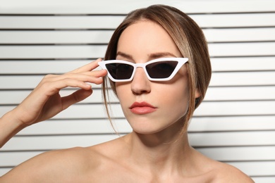 Photo of Young woman wearing stylish sunglasses against blinds