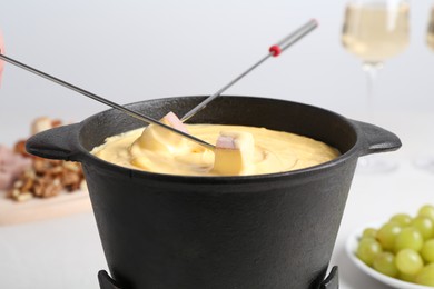 Photo of Dipping ham into fondue pot with tasty melted cheese at table, closeup