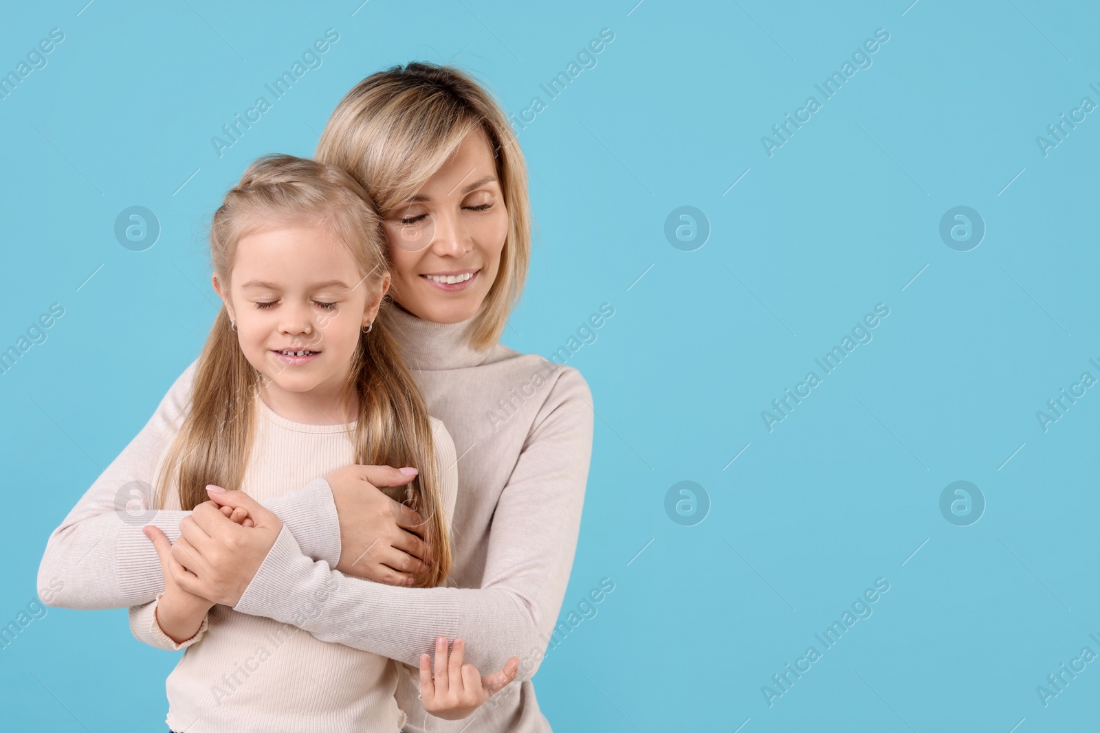 Photo of Mother hugging her happy daughter on light blue background. Space for text