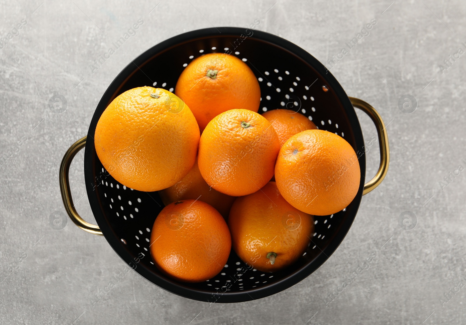 Photo of Fresh ripe oranges in black colander on light grey table, top view