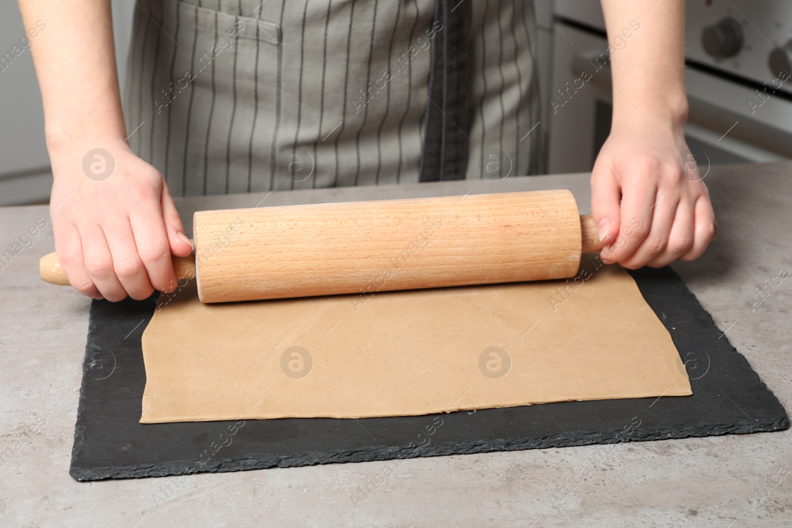 Photo of Woman rolling dough with wooden pin at table in kitchen, closeup