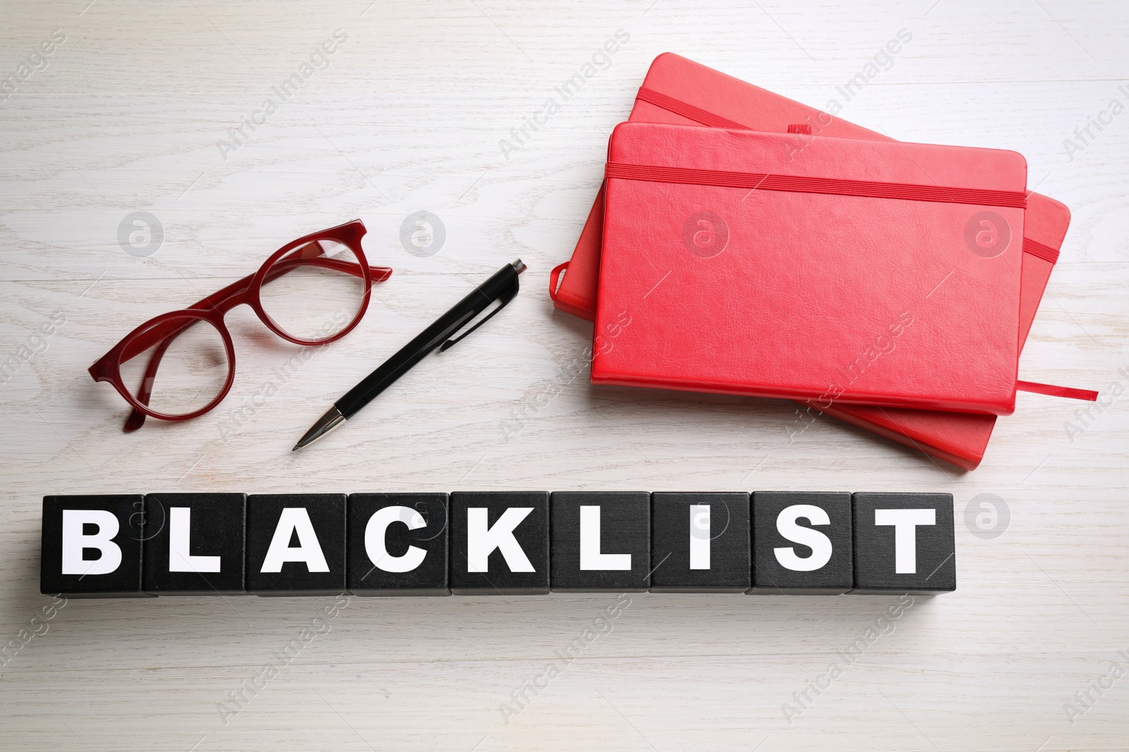 Photo of Black cubes with word Blacklist, glasses and office stationery on white wooden desk, flat lay