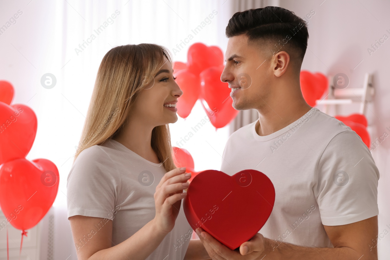 Photo of Lovely couple with gift in room. Valentine's day celebration