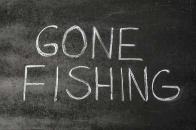 Photo of Words "GONE FISHING" written with chalk on dark blackboard