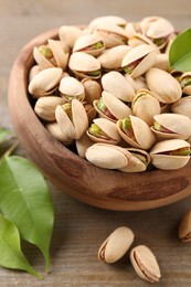 Photo of Delicious pistachios in bowl on wooden table, closeup