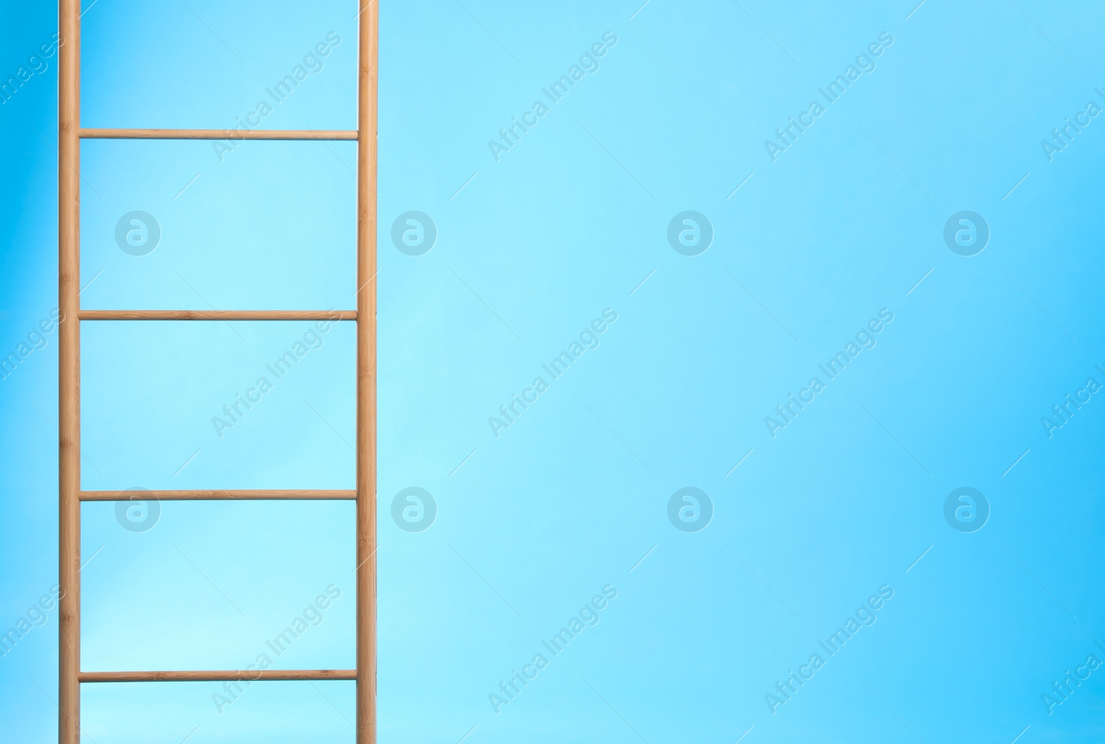 Photo of Modern wooden ladder on light blue background. Space for text