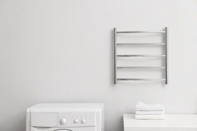 Photo of Heated towel rail on white wall in bathroom, space for text