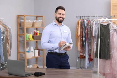 Photo of Dry-cleaning service. Happy worker taking notes in workplace indoors