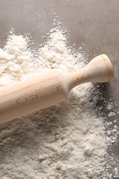 Photo of Scattered flour and rolling pin on grey textured table, top view