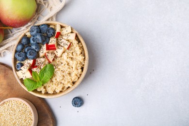 Photo of Bowl of delicious cooked quinoa with apples, blueberries and chia seeds on light grey table, flat lay. Space for text