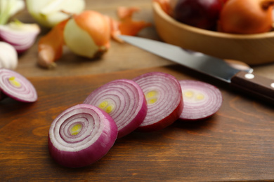 Photo of Sliced red onion and knife on wooden board, closeup