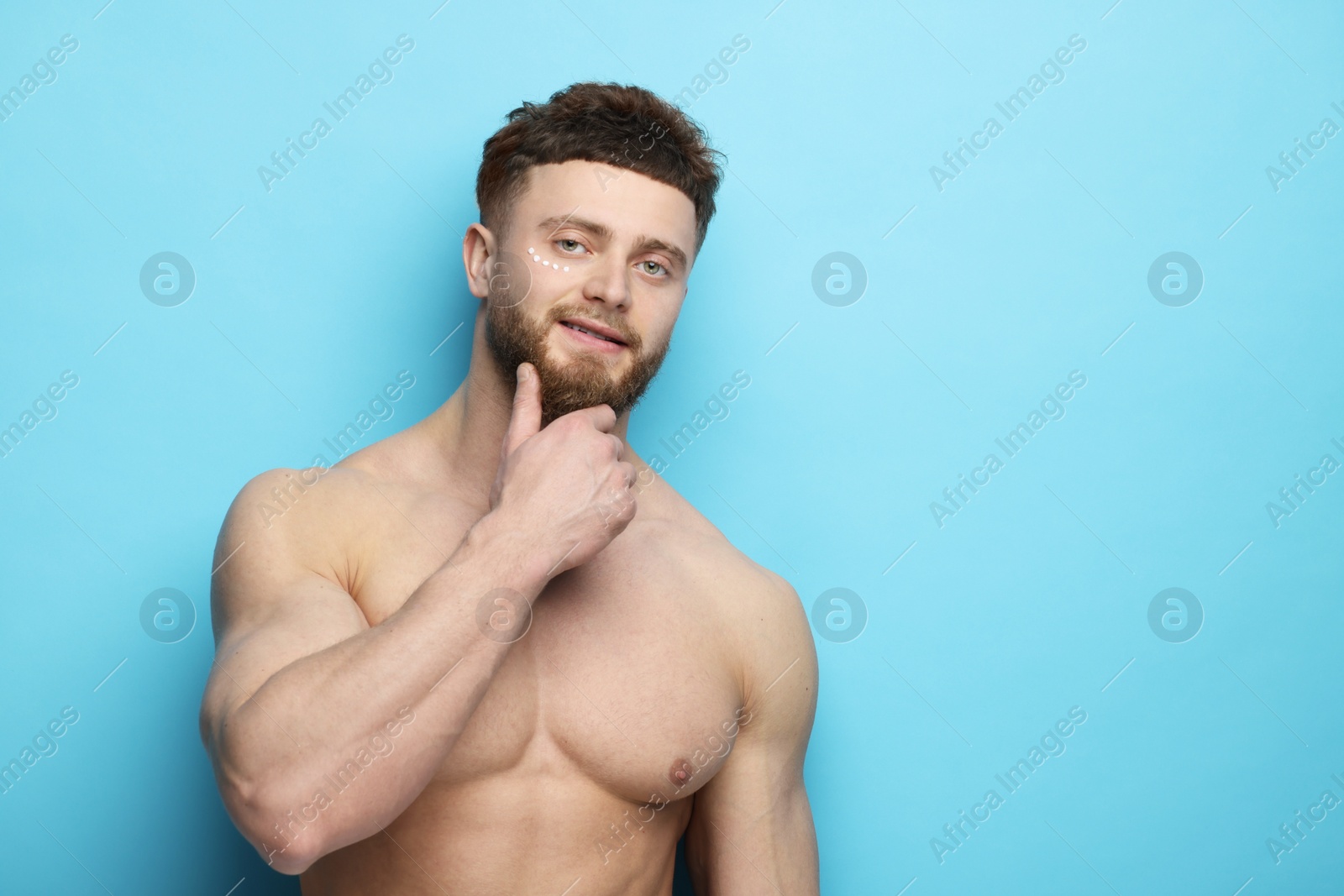 Photo of Handsome man with moisturizing cream on his face against light blue background, space for text