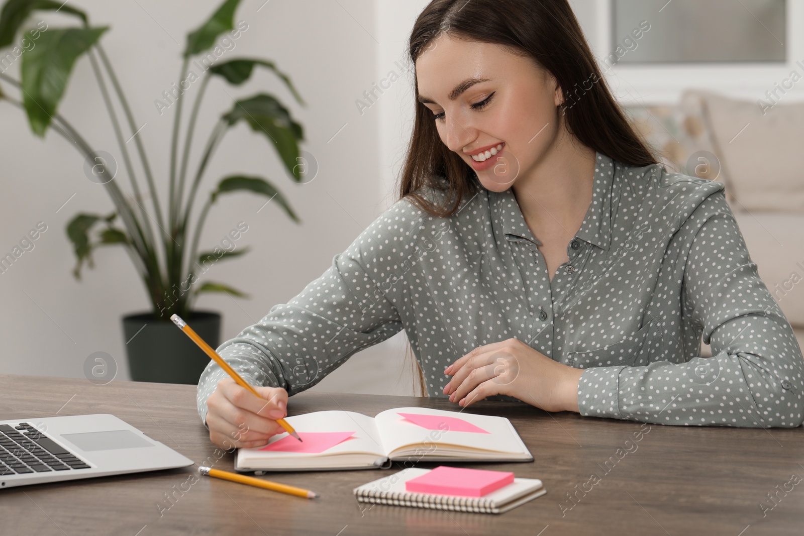 Photo of Woman with notebook and sticky note at wooden table indoors