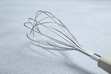 Photo of Metal whisk on gray table, closeup. Kitchen tool