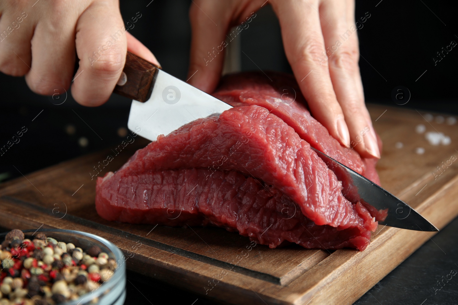 Photo of Woman cutting fresh raw meat at black table, closeup