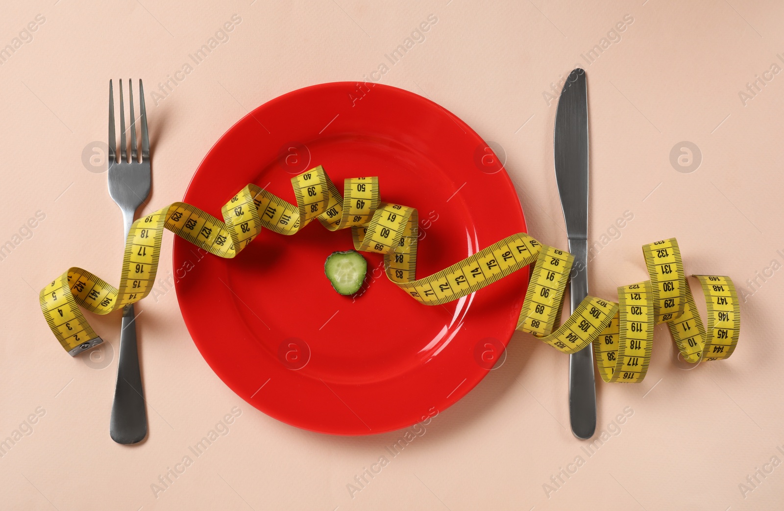 Plate with cucumber slice, cutlery and measuring tape on beige background, flat lay. Diet concept Photo of Plate with cucumber slice, cutlery and measuring tape on beige background, flat lay. Diet concept