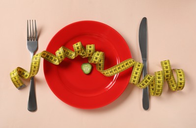 Photo of Plate with cucumber slice, cutlery and measuring tape on beige background, flat lay. Diet concept