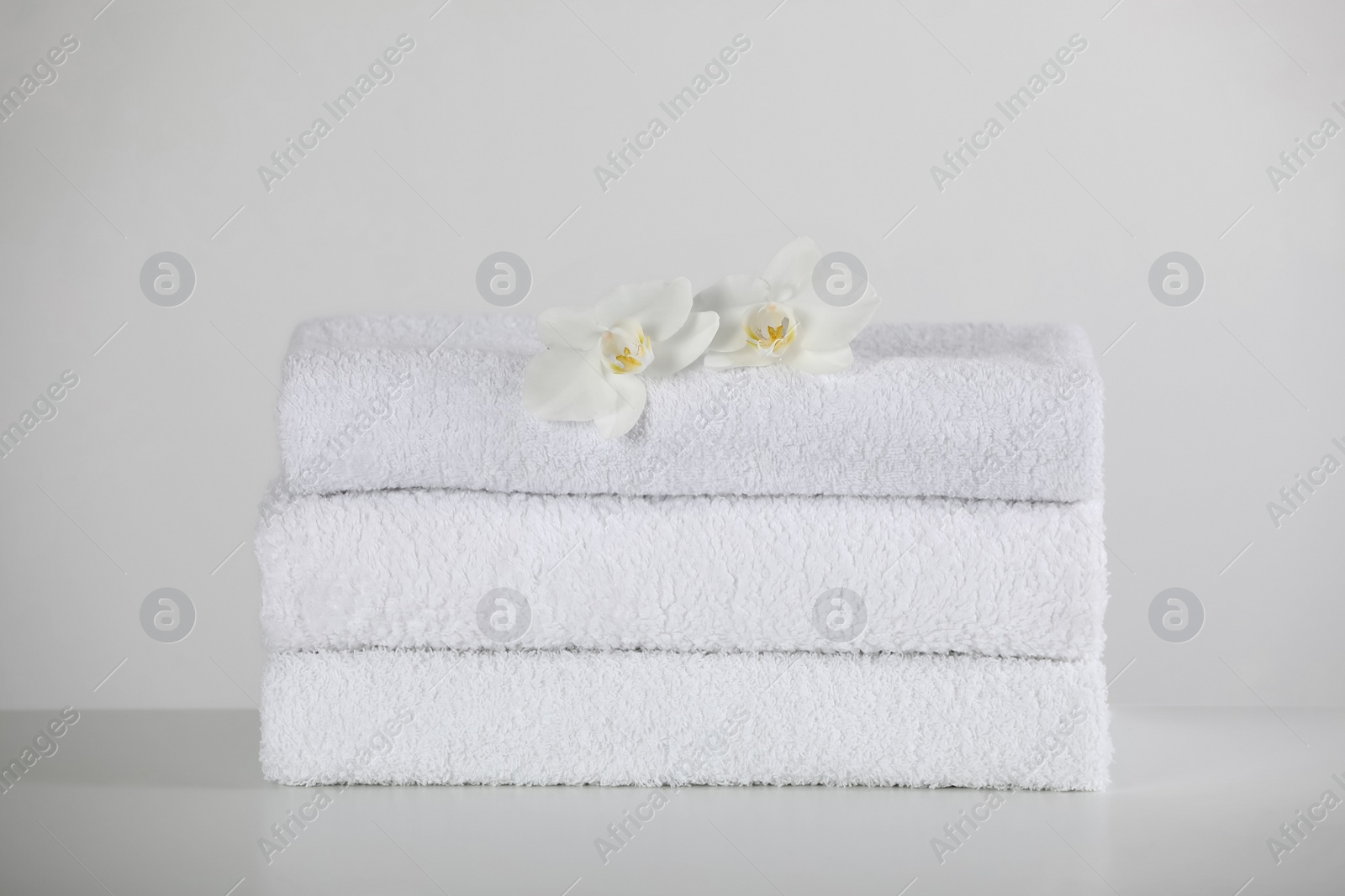 Photo of Soft folded towels and orchid flowers on white table