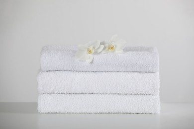 Photo of Soft folded towels and orchid flowers on white table