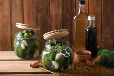Photo of Glass jars with fresh cucumbers and other ingredients on wooden table. Canning vegetable