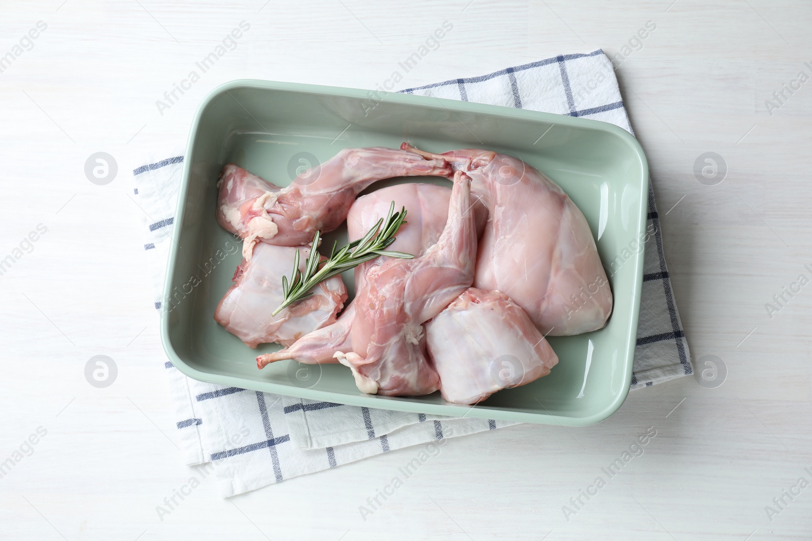 Photo of Raw rabbit meat and rosemary in baking dish on white wooden table, top view