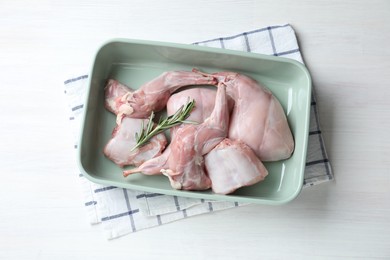 Raw rabbit meat and rosemary in baking dish on white wooden table, top view