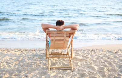 Photo of Young man relaxing in deck chair on beach near sea