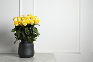 Photo of Beautiful bouquet of yellow roses in vase on light grey table near white wall, space for text