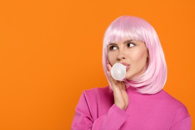Photo of Beautiful woman blowing bubble gum on orange background, space for text