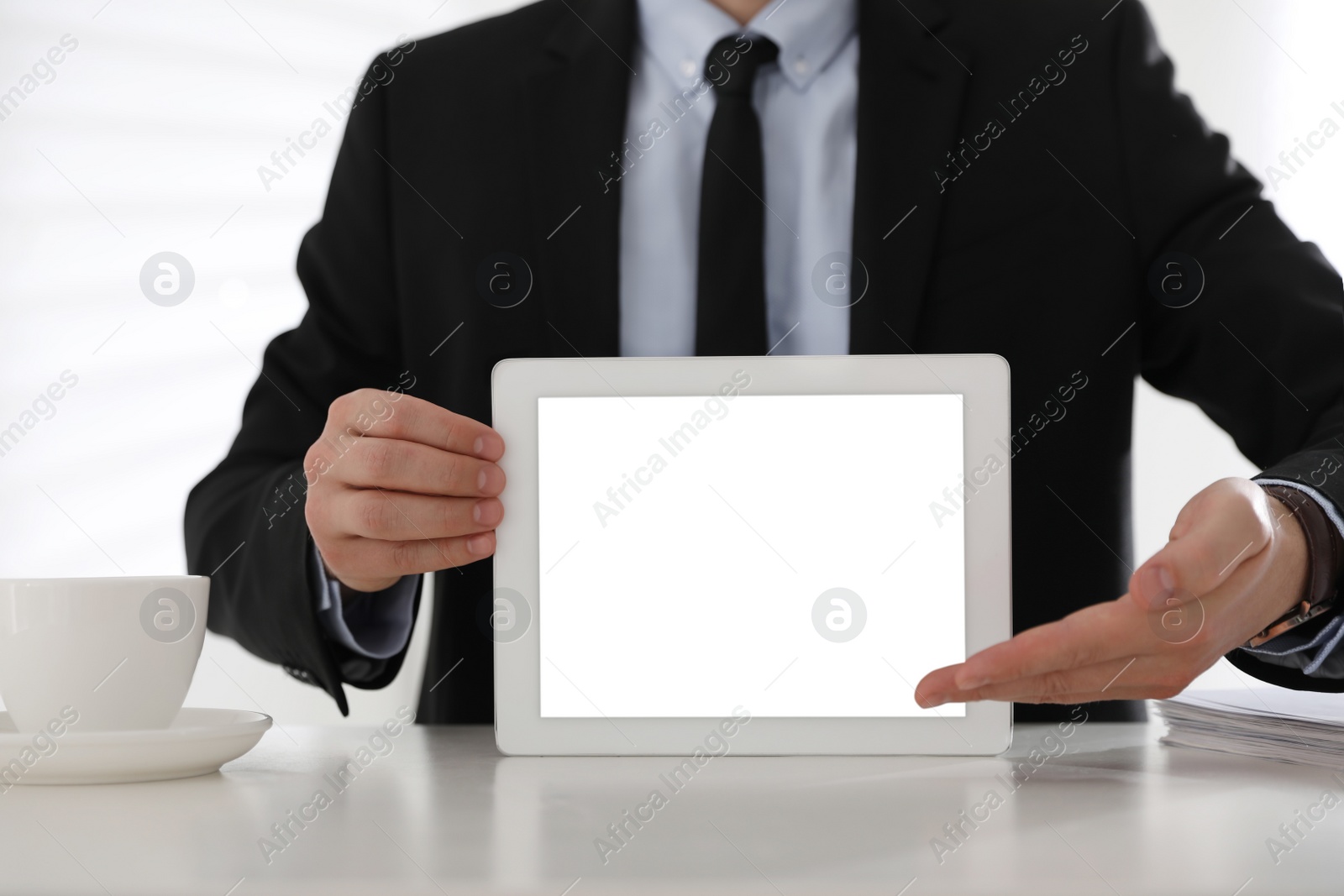 Photo of Businessman holding modern tablet with blank screen at white table in office, closeup