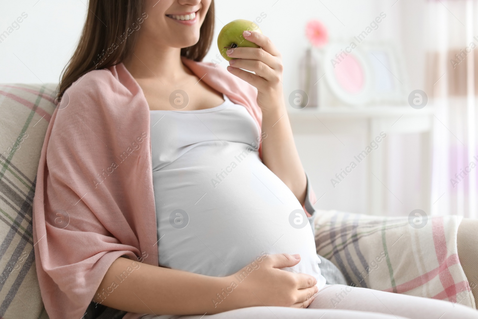 Photo of Young pregnant woman holding apple at home