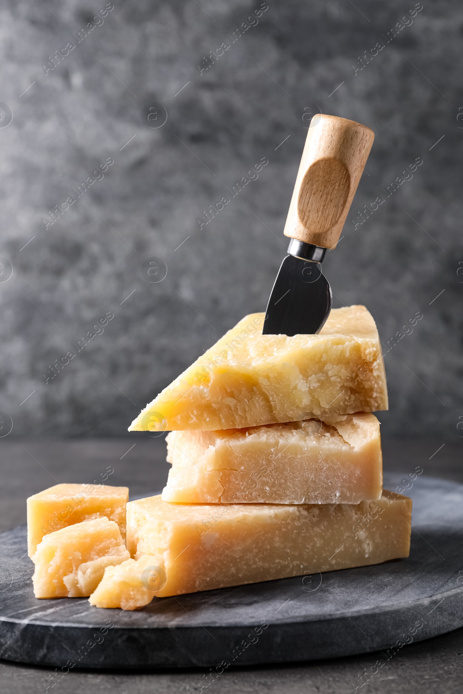 Photo of Parmesan cheese with board and knife on grey table