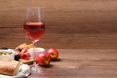 Photo of Glass of delicious rose wine and snacks on wooden table. Space for text