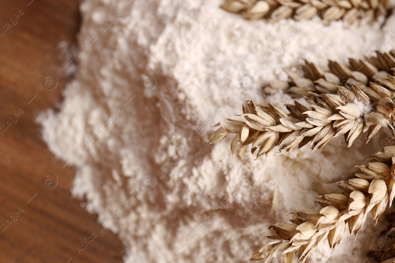 Photo of Pile of wheat flour and spikes on wooden board, closeup. Space for text