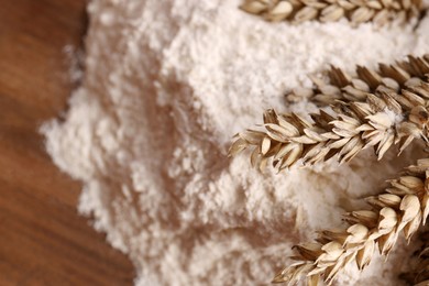 Pile of wheat flour and spikes on wooden board, closeup. Space for text