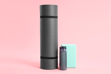 Photo of Grey exercise mat, yoga block and bottle of water on pink background