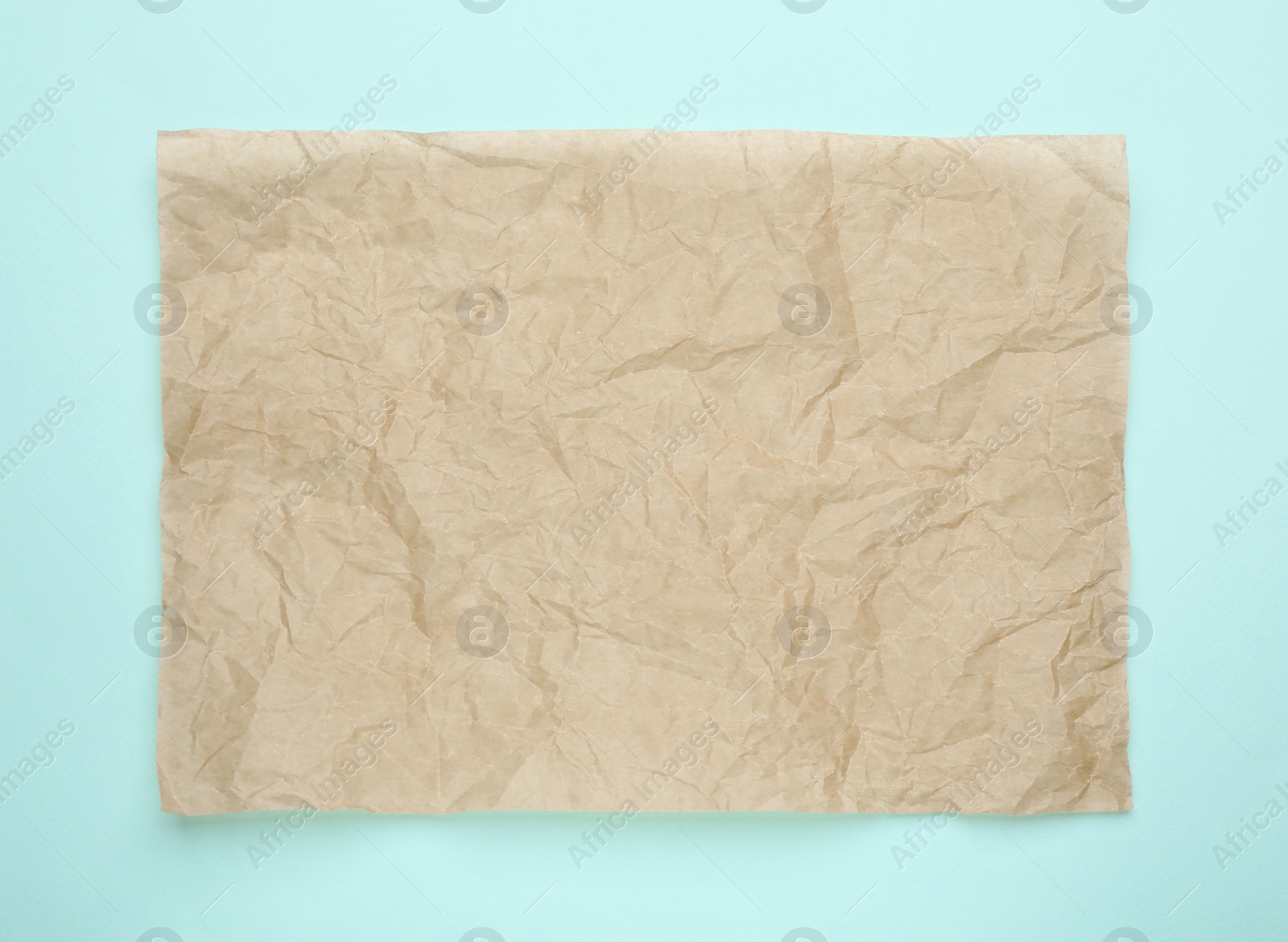 Photo of Sheet of crumpled brown baking paper on light blue background, top view