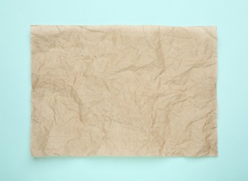 Photo of Sheet of crumpled brown baking paper on light blue background, top view