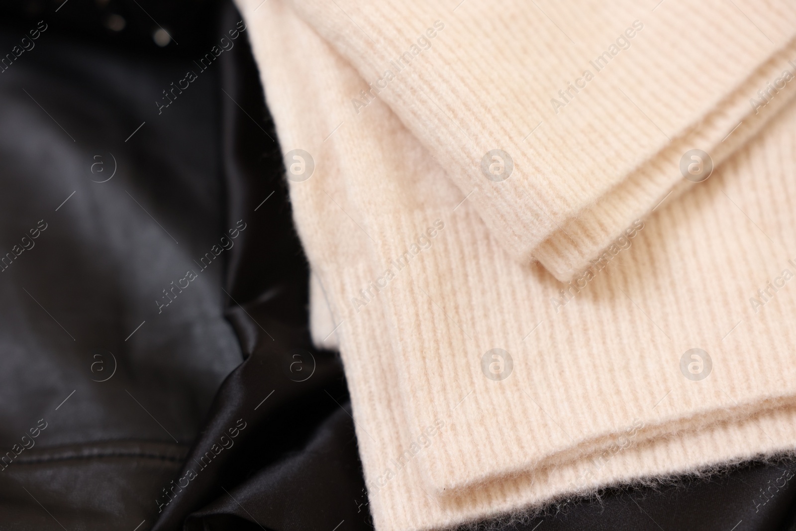 Photo of Soft beige sweater on black fabric, top view