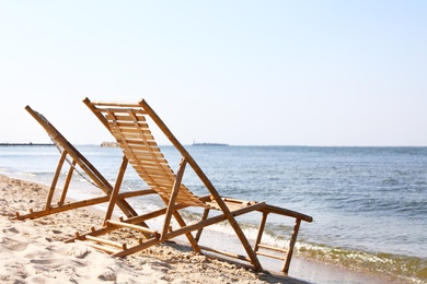 Sandy beach with empty wooden sunbeds on sunny day