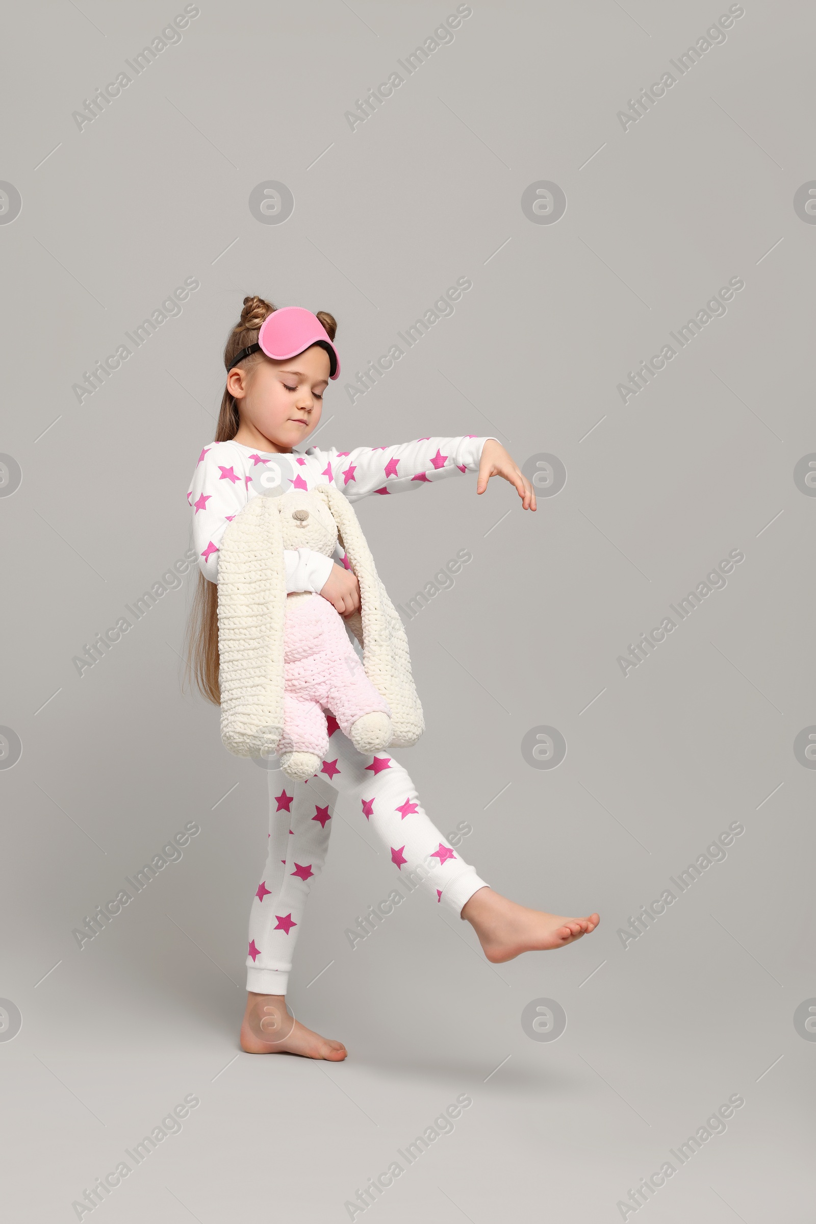 Photo of Girl in pajamas and sleep mask with toy bunny sleepwalking on gray background